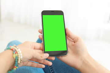 Woman holding smartphone with green screen indoors, closeup. Gadget display with chroma key. Mockup for design