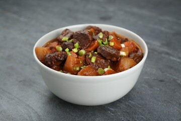 Delicious beef stew with carrots, green onions and potatoes on grey table, closeup