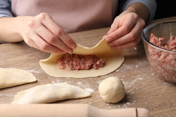 Woman making chebureki at wooden table, closeup