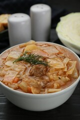 Tasty cabbage soup with meat, carrot and dill on black wooden table, closeup