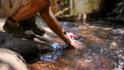 Cropped image of an Asian male trekker in trekking boots sitting by the mountain stream