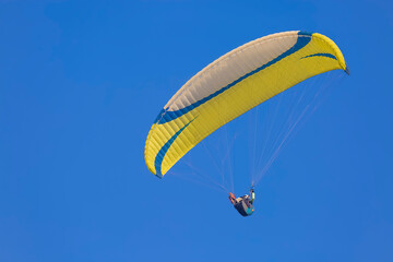 A yellow paraglider gliding across a clear blue sky