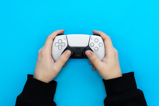 A male hands hold a gamepad on a blue background. Concept of the game, e-sports, leisure, gaming industry, video games, top view.