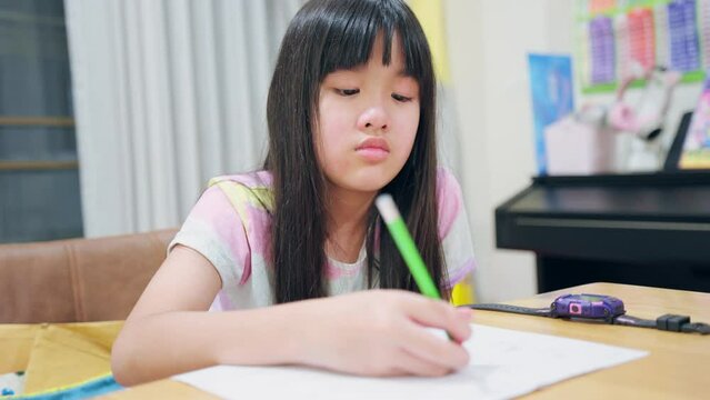 Asian young kid girl doing homework in living room at home on weekend. 