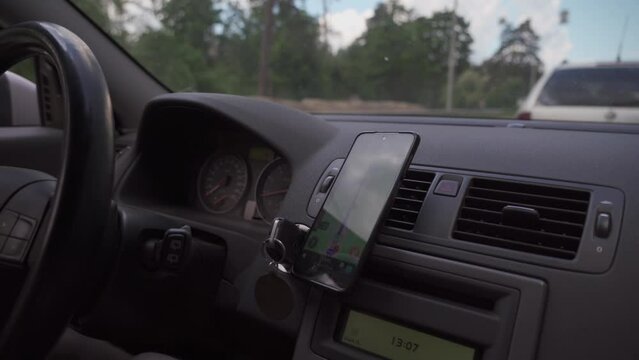 Driver using GPS navigation in mobile phone while driving car. map on the phone in the background of dashboard. Black mobile phone with map gps navigation fixed in the mounting. App map for travel.
