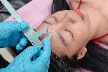 An esthetician uses a caliper to measure the length of the glabella or space between the eyebrows of a client. One of the first steps prior to a microblading procudure.
