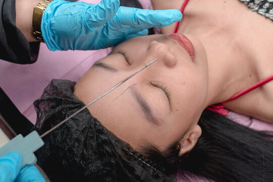 Using a thin rod to mark lines on a customer's face as a guide for for microblading procedure.