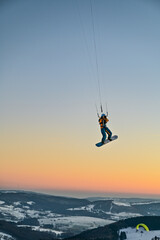 Snowkiting, snowboarder flies with a towing kite through the sunset in the sky of the Wasserkuppe in the Rhoen, Hesse, Germany