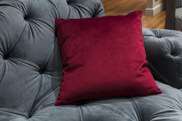 Burgundy throw pillow on a gray quilted modern sofa. Fashionable interior design and decor. Close-up.