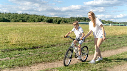 Fototapeta premium loving mother help her cute son ride a bicycle
