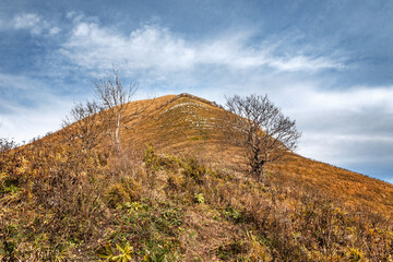 Large stones on the slope of Mount Peus. View of the mountain range under a cloudy sky. Dry grass on the slope of a high mountain. Panoramic view of the Caucasus mountains.