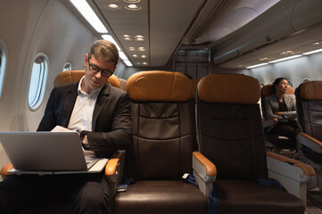 Businessman working on laptop while sitting in airplane cabin. Business work and travel concept.