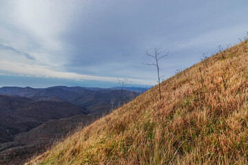 Dry grass on the slope of a high mountain. Landscape of a mountain range on an autumn morning. Panoramic view of the Caucasus mountains. View of the mountain range under a cloudy sky. 