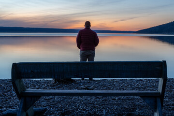 Winter scene of a man with red jacket along a beach looking out over a lake at a sunset.  Taking time for personal reflection, introspection, thinking about the past or the future.   