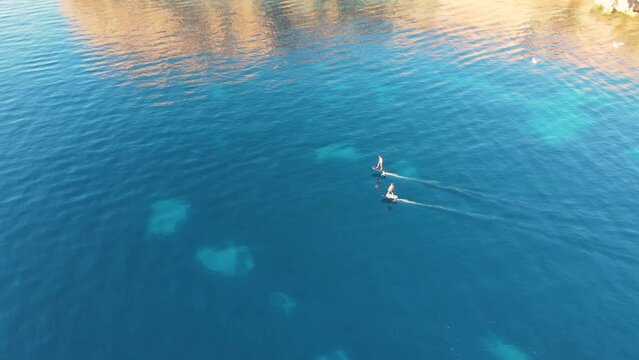Aerial View Behind Two People Surfing Across Waters Off Cala Escondida Coastline On Electric Surfboards. Dolly Tracking Shot