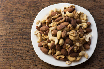 Mixed nuts on a white dish close up. Almond, walnuts, and cashew nuts on plate, placed on a rustic wooden table. shallow depth of field.