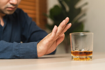 Alcoholism, depressed asian young man refuse, push out alcoholic beverage glass, drink whiskey, sitting alone at night. Treatment of alcohol addiction, having suffer abuse problem alcoholism concept.
