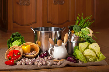 Still life with crockery and a variety of fresh organic vegetables. Food and fresh raw vegetables arranged around the stainless steel pan
