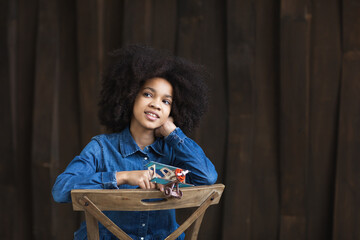 Fototapeta na wymiar Dreamy smiling african american girl in a denim shirt with an airplane model in her hands. Travel concept.