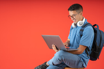 Happy young college man with glasses and white headphones on his neck, sitting using his laptop