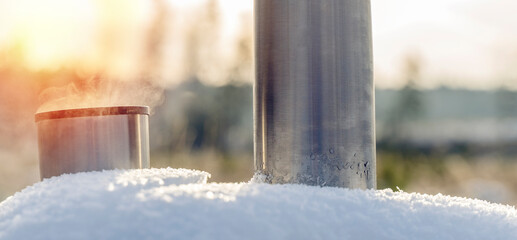Metal thermos with a hot drink on the background of a winter mountain waterfall. Insulated drink container in the snow