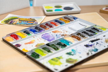 Colorful watercolor palette on table with watercolor set. Selective focus.