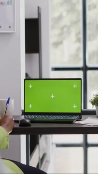 Vertical video: Executive assistant analyzing green screen display on pc, using laptop with chroma key copyspace display. Office employee looking at isolated mockup screen in business coworking space.