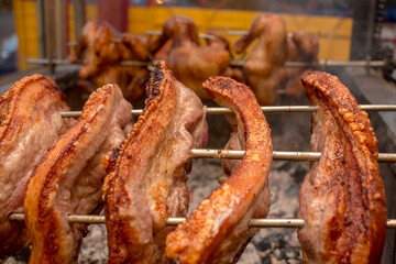 Several pieces of Liempo, or pork belly skewered on a spit and roasted on an oven at a roadside restaurant. Lechon manok in the back.