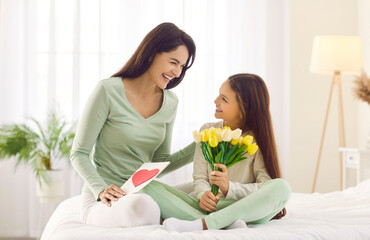 Obraz na płótnie Canvas Loving small girl child make surprise greeting happy mom with flowers and postcard with mothers day. Caring little daughter congratulate mum make surprise give present. Gratitude, bonding concept.