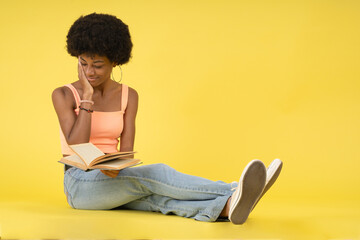 Young black lady with afro hairstyle, sitting on the floor sadly and emotionally reading a book