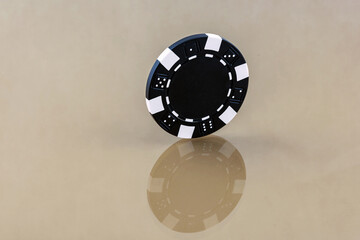 A black casino chip stands on the reflecting surface