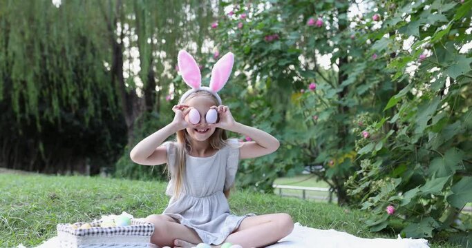 Adorable girl Wearing Bunny Ears when Pick Up painted Easter Egg Hunt In Garden or park. Cute caucasian child seven years old on backyard. Slow motion