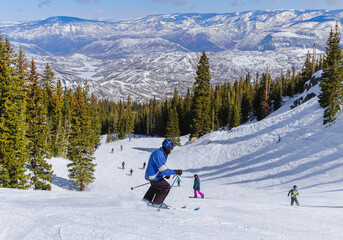 Senior male downhill skier skiing in Colorado ski resort on nice winter afternoon; forest and...