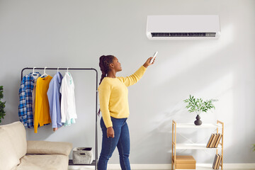 Young woman enjoys a modern air conditioning system at home. Happy beautiful African American woman...