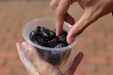 Close up of male hand holding date fruits with plastic food containers. Selective focus image