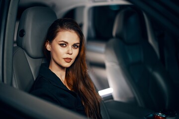a stylish, luxurious woman is sitting in a black car at night in the passenger seat, looking at the camera in a relaxed way. Topics of safe driving on the roads