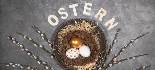 Frohe Ostern Feier Feiertage Hintergrund mit deutschem Text - Osternester mit gold bemalten Ostereiern und Palmkätzchen auf Tisch mit Beton Textur, Draufsicht
