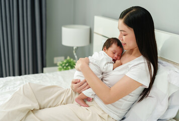 mother holding and consoling her newborn baby to sleeping on bed