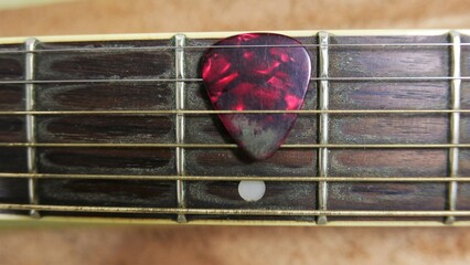 Top view: a guitar pick on a guitar neck. A guitar pick, close-up shot. A guitar neck, close-up...