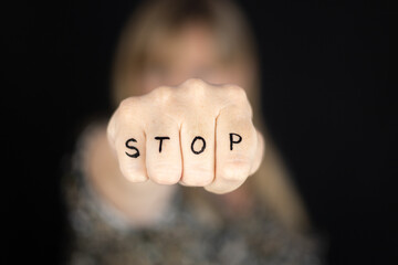 Woman with closed fist with word STOP written to campaign against gender violence and pain. Hand raised and punch to dissuade for self harm awareness, stop abusing, bullying, mental health. Copy space