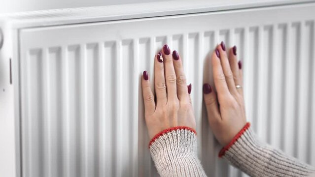 European woman hands in winter sweater warming touch home radiator feeling cold temperature 