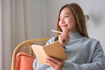 Portrait image of a young woman holding and writing on notebook at home