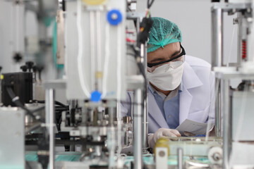 Naklejka premium Worker in personal protective equipment or PPE inspecting quality of mask and medical face mask production line in factory, manufacturing industry and factory concept.