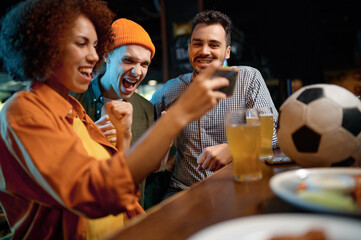 Cheerful friends having fun watching football game on smartphone at sport bar