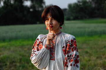Fototapeta premium A girl in a national dress on a background of greenery in a field on a sunny day