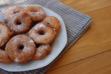 Homemade deep fried apple rings with batter sprinkled with powdered sugar ona white plate on wooden table