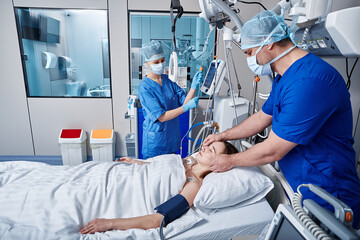 Intensive care patient. Nurses attending to female patient in intensive care unit of hospital