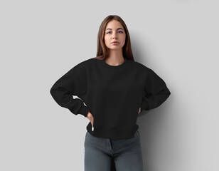 Template of a black cropped sweatshirt on a beautiful girl in jeans, with hands on her waist, textured wear isolated on background, front view.