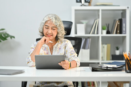 Pleasant middle aged woman surfing internet, reading online news on digital tablet. Elderly technology concept