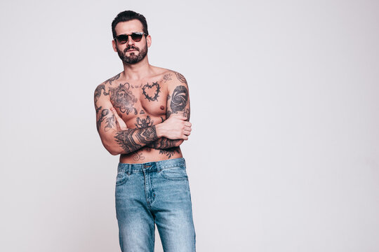 Portrait of handsome confident stylish hipster lambersexual model. Sexy modern man. Naked torso with tattoos.Fashion male posing in studio. Isolated on white. In sunglasses
